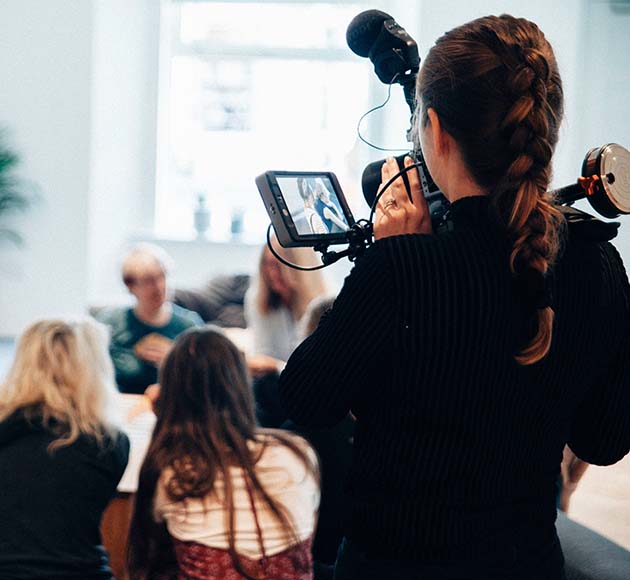 A camerawoman filming a scene in a living room using a professional camera.